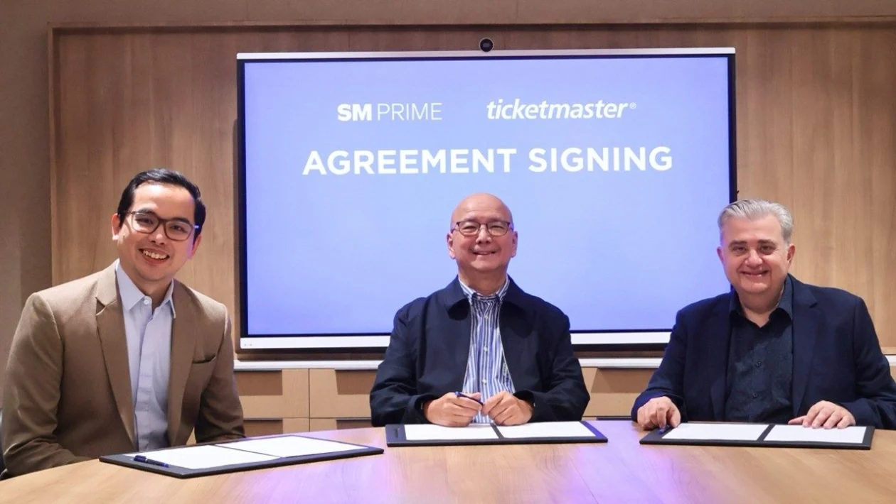SM Prime executives Cris Noel E. Torres and Jeffrey C. Lim sit with Ticketmaster APAC Regional Vice President Jim Kotsonis during an agreement signing, with a screen behind them showing the SM Prime and Ticketmaster logos.