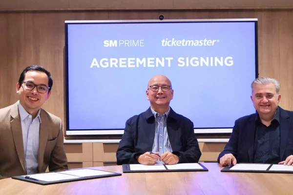 SM Prime executives Cris Noel E. Torres and Jeffrey C. Lim sit with Ticketmaster APAC Regional Vice President Jim Kotsonis during an agreement signing, with a screen behind them showing the SM Prime and Ticketmaster logos.