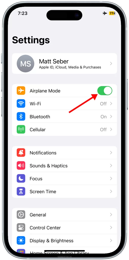 The image shows an iPhone 15 with the Settings menu opened and an arrow pointing to the Airplane Mode toggle switch that is enabled.